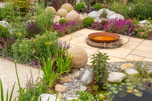 Gartenteich mit Steinumrandung, anliegender Terrasse und Feuerstelle